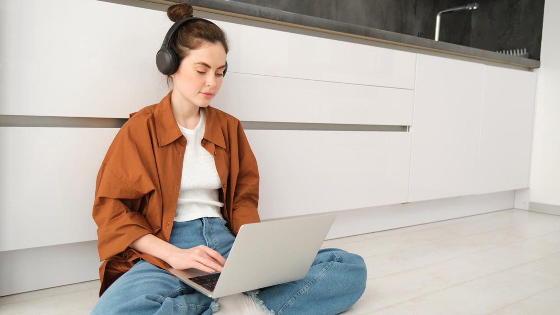 Frau sitz mit Laptop am Boden in der Küche. Frau sitz mit Laptop am Boden in der Küche.